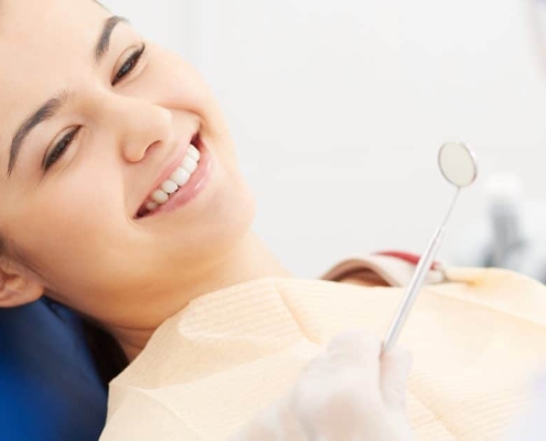 A woman sits in a dental chair smiling at a dentist who is holding a dental mirror.