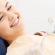 A woman sits in a dental chair smiling at a dentist who is holding a dental mirror.