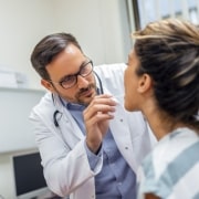 A doctor wearing a white coat examines a patients throat with a tongue depressor in a medical office.